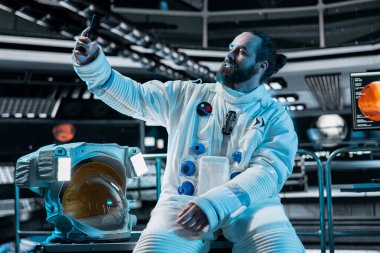 Gülümseyen kozmonot, arka planda Mars görev ekranı parlarken uzay istasyonunda selfie çekiyor. Mutlu uzay gemisi mürettebatı Red Planet 'e inmeden önce telefonla fotoğraf çekiyor.