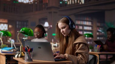 Dizüstü bilgisayarla eğitim belgeseli dinleyen ve notlar alan genç bir kız, üniversite kütüphanesinde ders çalışmak için geleneksel olmayan yöntemler kullanıyor. Bayan öğrenci veri topluyor. Kamera A.