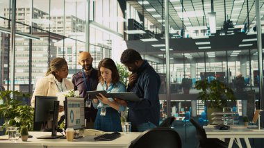 Çok ırklı iş arkadaşları çeşitli ofislerdeki tabletlerin gelir rakamlarına bakıyorlar. Çok ırklı iş arkadaşları beyin fırtınası yapıyor, şirketin istatistiksel rakamlarını karşılaştırıyor, işi bitirmek için çok çalışıyor, kamera B