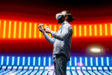 Neon ışıklı bir gece sahnesinde modern bir adam vr yüksek teknoloji gözlüğü kullanıyor, siber punk stilini somutlaştırıyor ve sanatsal vizyon yoluyla dijital ilham veriyor. Gelecekçi estetiğin parıldayan yansımaları.