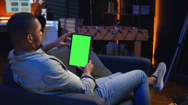 Siyah uzaktan kumandalı işçi evdeki cihazına bakıyor oturma odasında dinleniyor ve serbest çalışma görevlerini çözüyor. Adam modaya uygun bir dairede tele-çalışma yapıyor. Kamera A.