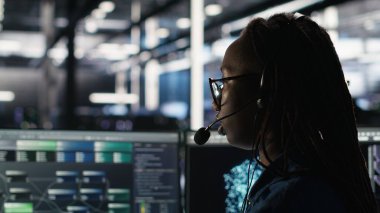 Veri merkezi uzmanı düğüm ağacı arayüzünü inceleyerek teknik destek sağlıyor. Sunucu odası teknisyeni iş arkadaşlarıyla mikrofonla konuşuyor, görsel programlama yazılımı kullanıyor, kamera B