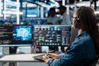 Veri merkezi destek uzmanı kulaklık mikrofonuyla konuşuyor, mühendislik ekibinin ekipman bakımını destekliyor. Sunucu çiftliğinde çalışan, mikrofon kullanan teknisyenler.