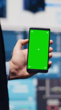 Dikey Video Erkek Yöneticisi dijital çalışma alanındaki yeni büyüme stratejisini anlamak ve analiz etmek için yeşil ekranlı telefonu kullanır. Modern iş zekasını ve verimliliğini temsil ediyor.
