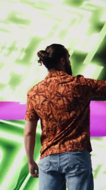 Dikey Video Genç kaygısız adam, modern DJ kültürünün, medya etkisinin ve dijital sanatın performansını temsil eden eğlenceli neon ışıklar ve ritimlerle çevrili selfie ve videolar çeker.