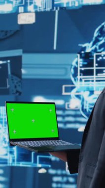 Dikey Video İş AI uzmanı beyin animasyonunun yanındaki cihazda yeşil ekran tutuyor ve sinirsel ağ sisteminin uygulanmasını sağlıyor. Algoritmaları ve kodlama araçlarını analiz eden genç bir uzman. Kamera B.