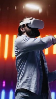 Sanatsal görüş yoluyla sanal gerçeklik gözlüklerini kullanarak, neon ışıklı bir gece sahnesinde yüksek teknolojili VR cihazına sahip dikey Video Young kişisi. Estetiğin parıldayan yansımaları