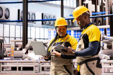 Kalite kontrol için tablet ve laptop kullanan akıllı üretim tesisinde mühendislik ekibi düzgün endüstriyel otomasyon sağlıyor. Teknisyenler akıllı fabrikada montaj bantları ve taşıma bantları yönetirler..