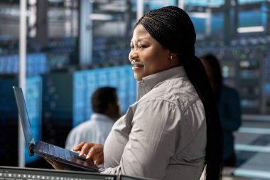 Sunucu odasında gülen teknisyen veri yedekleme çözümlerini uygulamak ve yönetmek için dizüstü bilgisayar kullanıyor. Happy Veri Merkezi Mühendisi teknik sorunları tespit ederek ve çözerek, verimli bir iyileşme sağlayarak