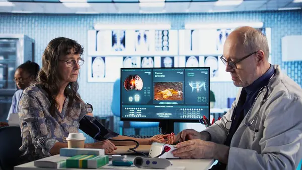 Klinik konsültasyonda profesyonel aletler kullanarak kan basıncını ölçen kıdemli bir doktor. Yaşlı doktor tansiyon ölçümü ve kalp atışı ölçümü yapıyor. Kamera A.