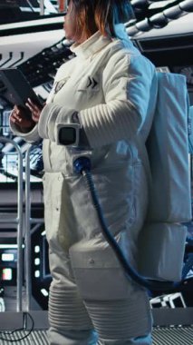 Yüksek teknolojili uzay aracının içinde miğfer tutan neşeli astronotların dikey video portresi rutin görev kontrolü sırasında ekipman çantasını tutuyor. Yıldızgemisindeki neşeli kadın monitörün yanında duruyor.