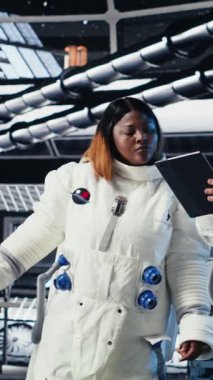 Yabancı gezegendeki yüzey görevini tamamladıktan sonra uzay istasyonunda miğfer tutan neşeli kadın astronotun dikey video portresi. Gülümseyen Afro-Amerikan kozmonot geri dönmeye hazırlanıyor.