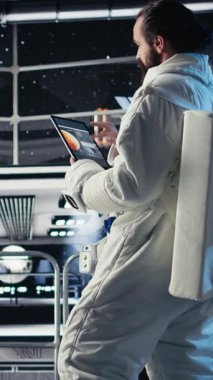 Uzay istasyonunun dışında planlanan operasyonlara çıkmadan önce kask takan astronotların dikey video portresi. Uzay gemisinde kozmonot kıyafetli bir adam uzak gezegen yüzeyine yaklaşıyor, kamera.