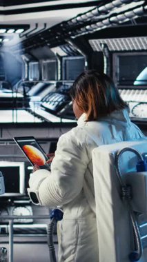 Dikey video Neşeli astronot elinde miğfer, uzayda uzay aracı kullanarak insan genleşmesi yapıyor. Yıldız gemisindeki mutlu Afrikalı Amerikalı kadın, insanoğlunun uzun vadede hayatta kalmasını destekleyen keşif gezisine hazırlanıyor.