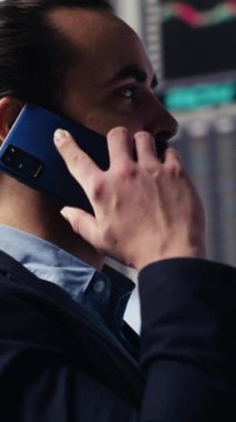 Vertical Video Expert iş adamı akıllı bir telefonla finans ve analizi tartışıyor, bir şirket stratejisi kuruyor. Veri tablolarıyla çevrelenmiş, dijital yenilik ve şirket büyümesi planlanıyor