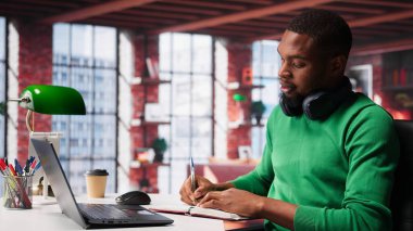 Gülümseyen siyah adam özel bir sunumu izlerken not alıyor, çevrimiçi olarak kendini öğreniyor ve detayları yazıyor. Genç yetişkin adam not defterine bir şeyler yazıyor. Kamera A.