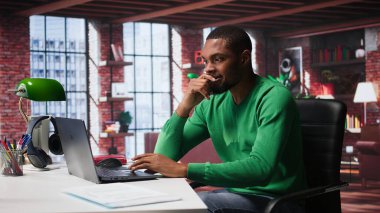 Uzaktan kumandalı çalışan siyahi bir adam masasında huzursuz ve endişeli bir şekilde bacaklarını sallıyor ve görev bitimi ve teslim tarihi nedeniyle gergin. Baskı ve endişe altında çalışan serbest çalışan biri. Kamera B.