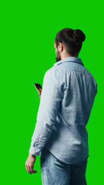 Dikey Video Gündelik stil adamı akıllı telefonuyla yeşil ekran arkaplanını tarıyor, sosyal ağ platformlarına bağlanıyor ya da mesajlaşıyor. Genç yetişkin sosyal medya uygulamalarına odaklandı