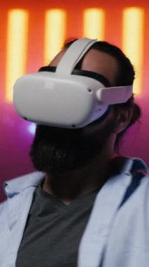 Dikey Video Modern Adam, VR yüksek teknoloji gözlüklerini kullanarak, sanal punk tarzını somutlaştırarak ve sanatsal vizyon yoluyla dijital ilham alarak, neon ışıklı bir gece sahnesinde. Gelecekçi estetiğin parıldayan yansımaları