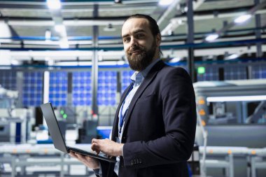 Güneş paneli endüstrisi uzmanı yüksek teknolojili bir tesiste denetleme ve kalite kontrol üretim ölçümlerinde duruyor. Yenilik için endüstriyel operasyonları güvence altına alan profesyonel danışman.