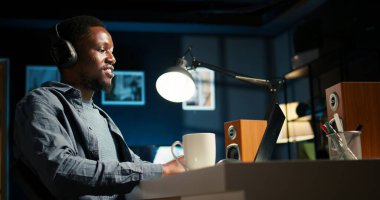 Afrikalı Amerikalı adam uzaktan kumandalı iş yapıyor ve web sohbeti yapıyor, bilgisayarını kullanarak oturma odasındaki bir online video görüşmesine katılıyor. Genç adam bir konferansa katılıyor. Kamera A.