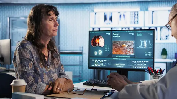 Doktor, ofisteki bir hastaya kanser taraması rehberliği yapıyor, MRI taramaları ve tümör büyümesini tartışıyor. Erken teşhis ve önleyici ilaçlar daha iyi sağlık sonuçları için vurgulanmaktadır. Kamera A.