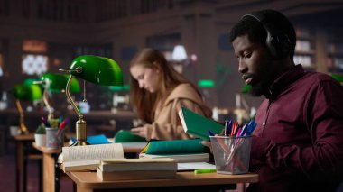 Siyahi adam akademik başarıya odaklanmak için çalışma müziğini kullanıyor, güvenilir kaynaklar bulmak için kampüs üniversite veritabanına başvuruyor. Erkek üniversite öğrencisi diploma için savaşıyor. Kamera A.