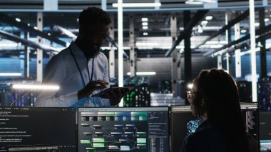 Sunucu merkezi yöneticisi sistem sağlığını optimize etmek için düğüm ağacı yazılımı kullanarak programcıyla konuşuyor. Veri Merkezi Yöneticisi, Yapay Zeka görselleme, Kamera B kullanılarak ekipman sorunlarını analiz eden bilişim uzmanı.
