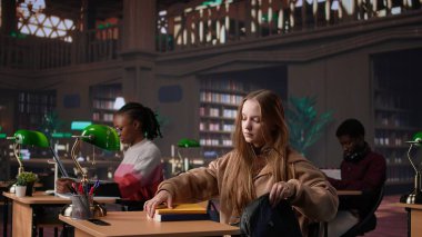 Bayan üniversite öğrencisi yeni bir ders için ayrıntılı notlar okuyup yazıyor, üniversitedeki kütüphane ortamında verilecek bir ders için siyaset bilimi okuyor. Kız danışmanlık veritabanı. Kamera B.