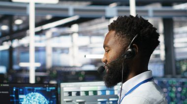 Veri merkezi çalışanı mikrofonla konuşuyor, koordine teknisyenler yapay zeka konuşlandırması için donanım kuruyor. Sunucu odası çalışanı, mühendisler ve kamera B ile bağlantı kuruyor.