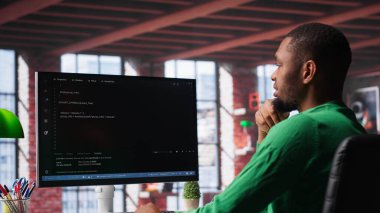 Merkez ofisteki siyah teknisyen UI 'ye bilgisayar monitöründe bakar, programlama kodunu yazar ve çalıştırır. Modern dairede kodlama uygulaması kullanarak kod yazıp test eden bilişim işçisi. Kamera A.