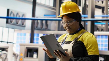 Akıllı fabrikadaki gülümseyen mühendis tablet kullanarak tahmin yürüterek IoT sensör verilerini analiz ediyor. Fotovoltaik sistemlerin işlevsel güvenilirliğini yöneten endüstriyel fabrika işçisi, kamera B