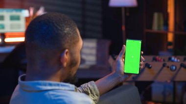 Afro-amerikan genç yetişkin kanepeye uzanmış, evinde esnek çalışma saatleriyle mutlu ve rahat hissediyordu. Freelancer oturma odasında telefon dinlendirici kullanıyor. Kamera B.