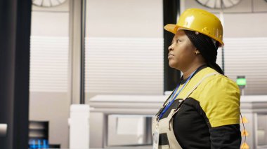 Endüstriyel fabrikada yürüyen teknisyenler, ekipman hatalarını teşhis etmek ve düzeltmek için alet kutusunu kullanıyorlar. Üretim fabrikasındaki Afrikalı Amerikalı kadın koordinatları montaj hatlarındaki tamir görevleri, kamera B
