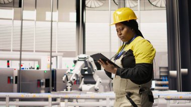 Mühendis fotovoltaik fabrikasında yürüyor, tabletteki sistem performans ölçümlerine bakıyor. İşçi sektörü 4.0 fabrika işletiyor, IoT sensörleri, kamera A aracılığıyla enerji üretimini takip etmek için aygıt kullanıyor.