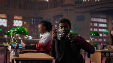 Afrika kökenli Amerikalı erkek öğrenci el yazısı sınıf notlarıyla ders kitabını tamamlıyor, üniversite kütüphanesindeki özel kitaplardan bilgi okuyor. Genç yetişkin danışmanlık veritabanı. Kamera A.