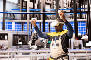 Akıllı imalat santralindeki siyah erkek mühendis üretimi ve kalite kontrolünü izlemek için sanal gerçekliği kullanıyor. Otomatik fabrika yapay zeka, endüstriyel otomasyon ve yeşil teknolojiyi birleştiriyor..