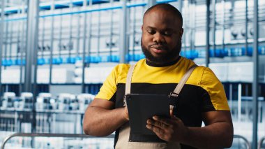 Akıllı fabrika mühendisi tesis katındaki robot silah ve montaj hatlarını denetliyor. Endüstri 4.0 Afro-Amerikan erkeği sistem performansını izliyor ve sorun yaratıyor, kamera A