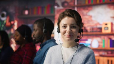 Ofisteki müşterilere yardımcı olmak için kulaklık takan neşeli bir çağrı merkezi çalışanı. İş yerindeki neşeli kadın müşteri desteği alıyor, müşterilerle telefon görüşmesinde iletişim kuruyor, kamera kapanıyor.