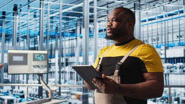 Akıllı fabrika mühendisi tesis katındaki robot silah ve montaj hatlarını denetliyor. Endüstri 4.0 Afro-Amerikan erkeği sistem performansını izliyor ve sorun yaratıyor, kamera A