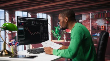 Afro-Amerikalı bir adam hisse senedi alıp satmak için PC 'yi kullanıyor. Forx grafiklerini ve diyagramlarını izliyor. Borsada çalışan bir borsa simsarı bilgisayardaki mum çubuğu çizelgelerine bakıyor. Kamera B.