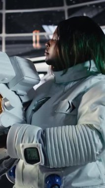 Uzay giysisi içindeki dikey video kadın astronot uzayda insan genleşmesi yapan uzay aracının içindeki bilek cihazını kontrol ediyor. Yıldız gemisi mürettebatı, insanoğlunun uzun vadede hayatta kalmasını destekleyen operasyonlara hazırlanıyor.