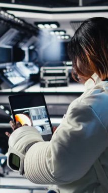 Yabancı gezegendeki yüzey görevini tamamladıktan sonra uzay istasyonu analizlerini kontrol etmek için tablet kullanan dikey video kadın astronot. Kadın navigasyon koordinatlarını giriyor, dönüş için hazırlanıyor