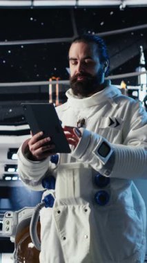 Uzay giysisi içindeki dikey video kadın astronot uzay aracının içindeki tablette insan genişlemesini kontrol ediyor. Yıldız gemisindeki kadın, insanoğlunun uzun vadede hayatta kalmasını destekleyen keşif seferine hazırlanıyor.