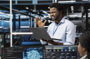 Yapay zeka ve makine eğitimini çalıştırmak için gerekli olan veri merkezi ekipmanlarının arızalanmasına sinirlenmiş bir teknisyen. Yapay zeka araçları kullanırken hatalar tarafından rahatsız edilen sinirli sunucu oda çalışanı