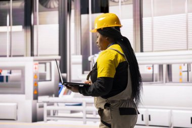 Kadın mühendis endüstriyel otomasyon sistemi ile çalışıyor. Burada akıllı üretimler otonom robotik kolları, dijital kontrolleri ve en yüksek verimlilik için optimize taşıma bandı operasyonlarını birleştiriyor..