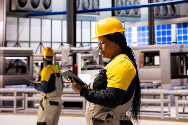 Endüstriyel teknisyen akıllı fabrikada üretimi ve güneş enerjisi sistemlerini denetliyor. Siyah kadın mühendis sanayi 4.0 enerji santralindeki tablet üretim sürecini inceliyor.