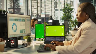 Ofis masasında bilgisayardaki belgeleri düzenleyen çalışanın yanında izole ekran bilgisayarı ve tablet var. Veri tablolarını analiz eden, istatistiksel bilgileri yorumlayan işçinin yanındaki krom anahtar cihazlar, kamera B