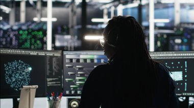 Yapay zeka analizi grafiklerini yorumlayan sunucu odası programcısı, kulaklık takıyor. Veri merkezi bilişim uzmanı sistem ölçümlerini, dinleme müziğini, kamera B 'yi gösteren yapay zeka aracı kullanıyor