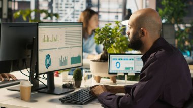 Ofis masasındaki masaüstü bilgisayarında dosya düzenleme, raporlar ve dosyalar güncelleniyor. İşçi masadaki bilgisayar ekranında veri tablolarını analiz ediyor, istatistiksel bilgileri yorumluyor, kamera A